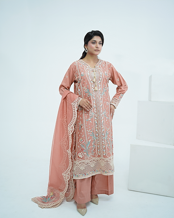 A model wearing a peach embroidered lawn Eid dress with intricate boring design and organza border, paired with a cotton net dupatta with embroidered borders – Amzoclothing festive collection.