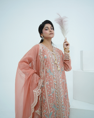 A model wearing a peach embroidered lawn Eid dress with intricate boring design and organza border, paired with a cotton net dupatta with embroidered borders – Amzoclothing festive collection.