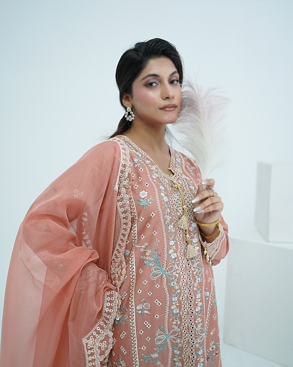A model wearing a peach embroidered lawn Eid dress with intricate boring design and organza border, paired with a cotton net dupatta with embroidered borders – Amzoclothing festive collection.