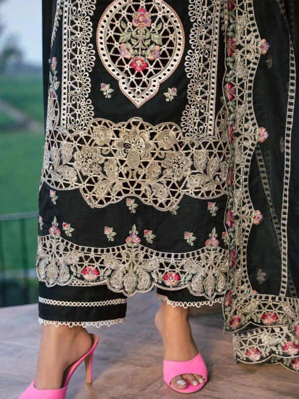 Woman wearing an elegant black embroidered long dress with beige and pink floral detailing, styled with gold clutch and pink heels