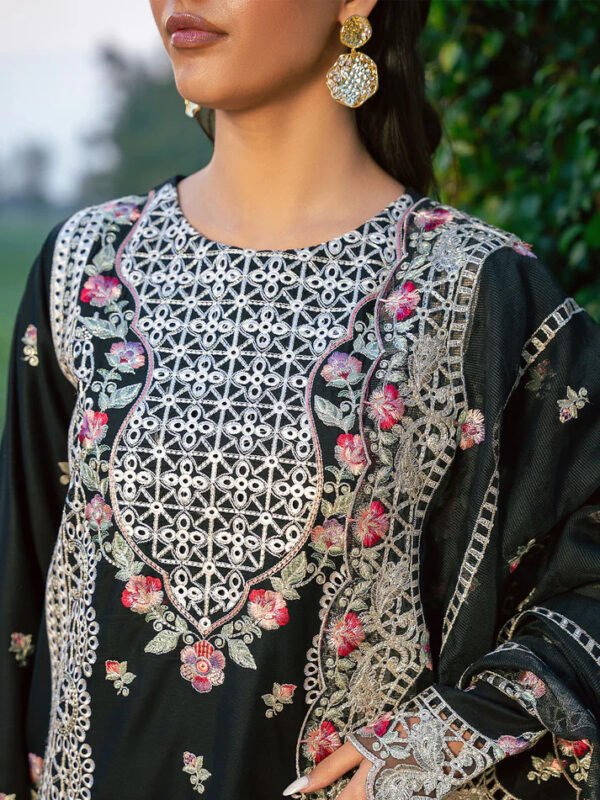 Woman wearing an elegant black embroidered long dress with beige and pink floral detailing, styled with gold clutch and pink heels
